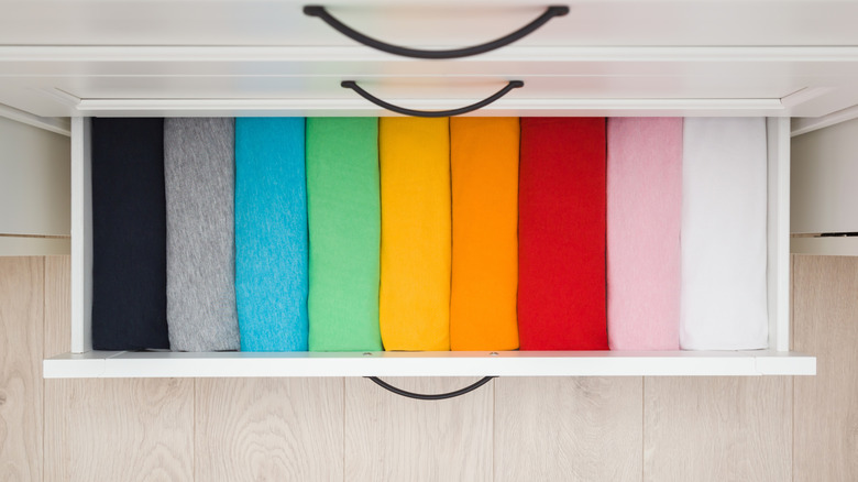 An open drawer full of rolled up different colored t-shirts.