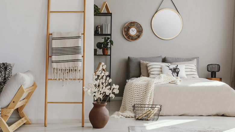 A blanket ladder in a Scandinavian-style bedroom with low double bed with cream and gray bedding.