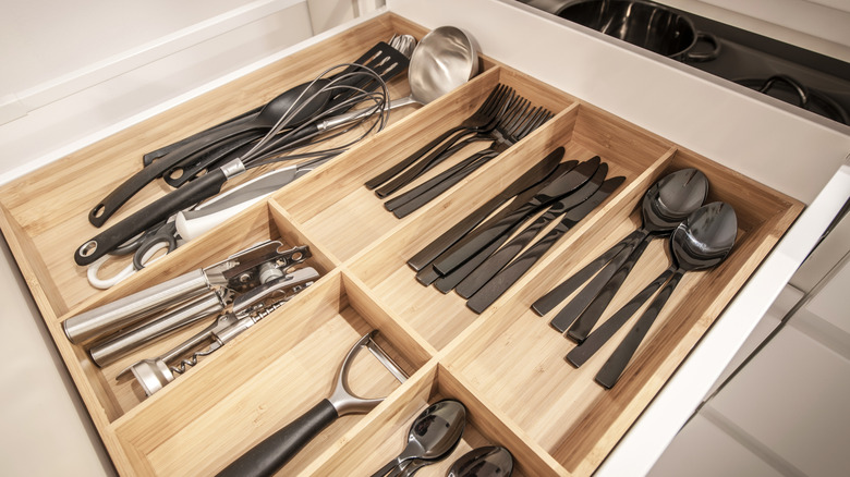 A kitchen drawer with a drawer divider and cutlery and utensils carefully arranged in the compartments.