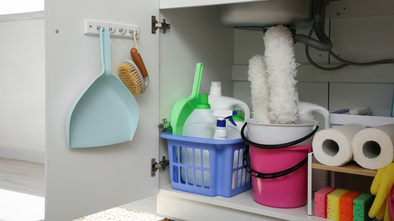 A neatly arranged under the sink cupboard with caddies and buckets to hold cleaning products.