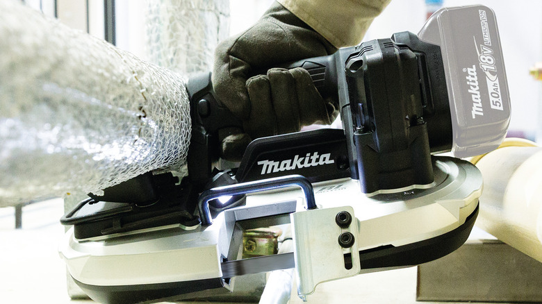A person using Makita's 18V LXT Sub-Compact Brushless Cordless Band Saw to cut metal pipe