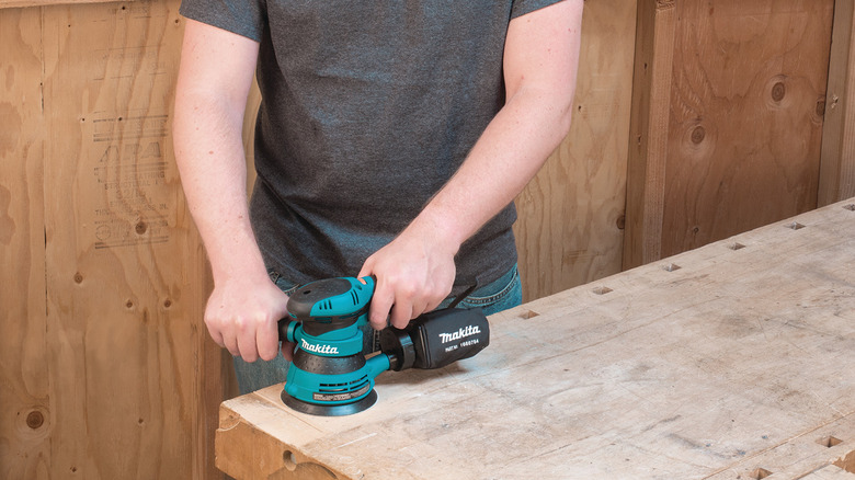 A person sanding a wooden surface with Makita's 3-Amp 5-inch Corded Variable Speed Random Orbital Sander