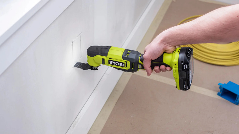 A person cutting out an electrical outlet hole in a wall with Ryobi's 18V One+ Cordless Oscillating Multi-Tool