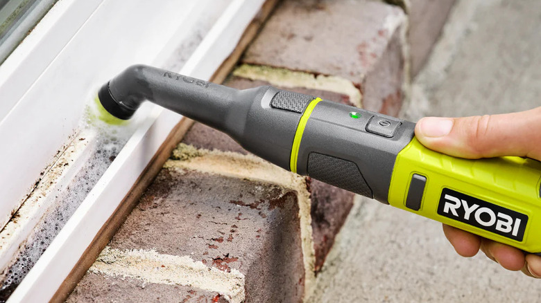 A person cleaning a PVC door frame with Ryobi's USB Lithium Cordless Compact Detail Scrubber Kit