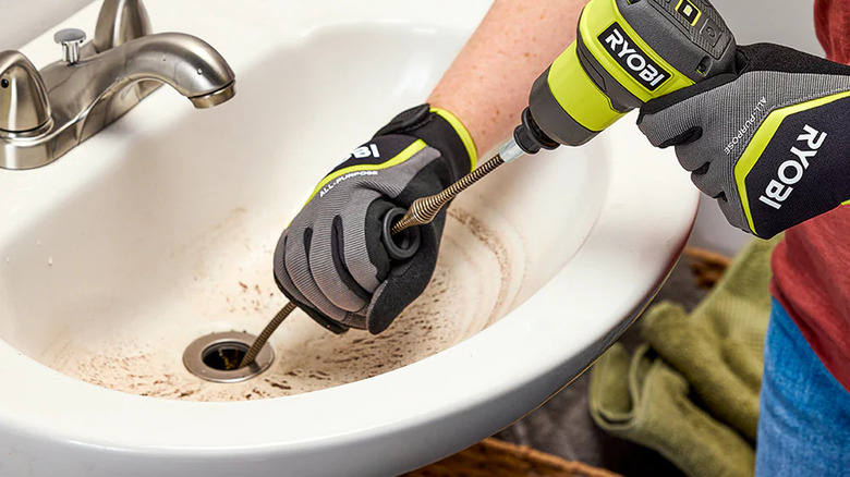 A person clearing a sink blockage with Ryobi's USB Lithium Cordless Drain Auger