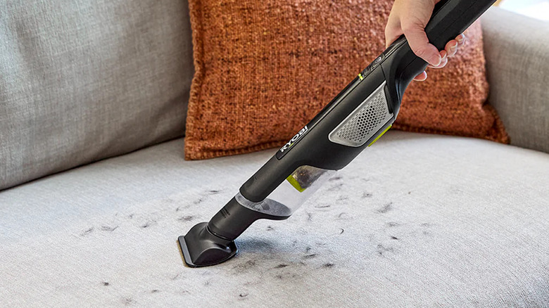 A person cleaning a sofa with Ryobi's USB Lithium HP Compact Hand Vacuum Cleaner