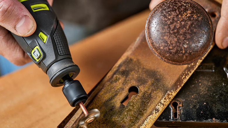 A person cleaning a rusty door handle with Ryobi's USB Lithium Rotary Tool Kit