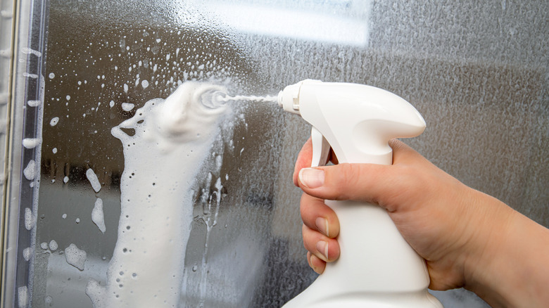 Close shot of a hand applying a spray to a glass shower door