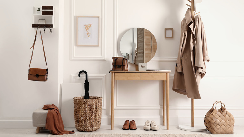 An entryway drop zone with: a purse and keys on hooks, a side table with a purse and tablet on top and shoes underneath, a coat rack, and umbrella in a basket