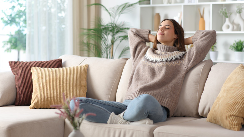 Woman with arms behind her back relaxing and looking blissful on a tan couch in a tidy living room