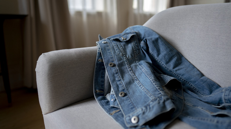 A blue jean jacket laying on a gray couch