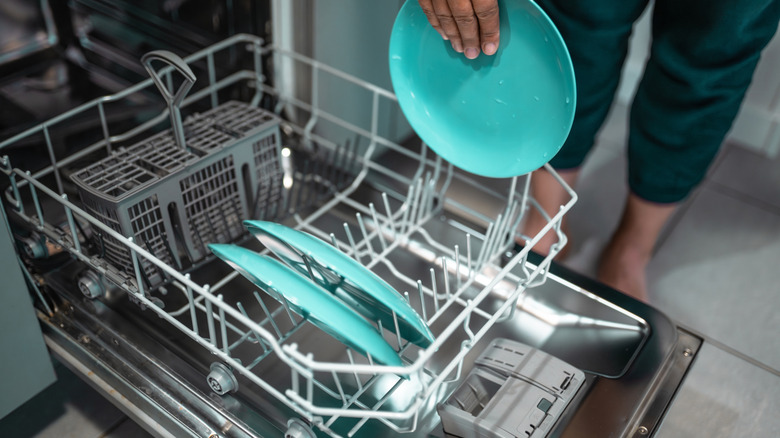An angled overview shot of rinsed teal dishes being loaded into a dishwasher