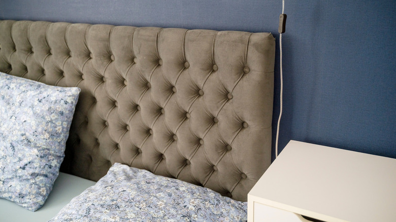 A large brown velvet headboard with two floral pillows below it.