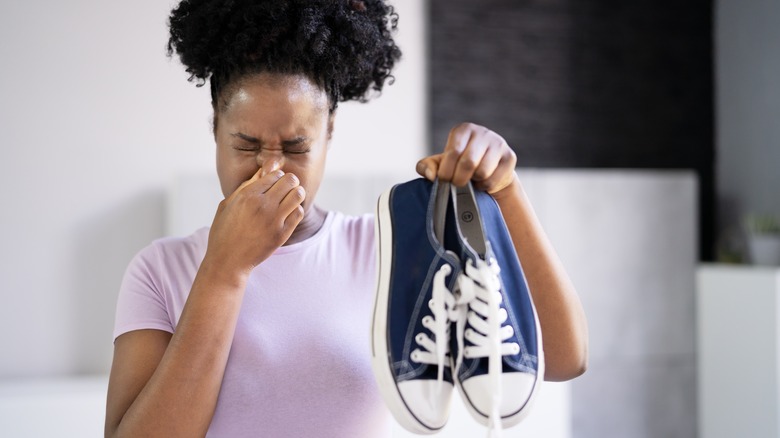 A woman holding her nose with a smelly pair of trainers in her hands.