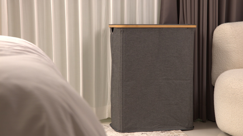 A tall slate colored laundry basket in a bedroom.