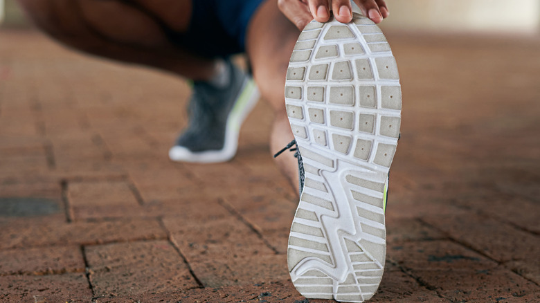 A person stretching and revealing the bottom of their running shoes