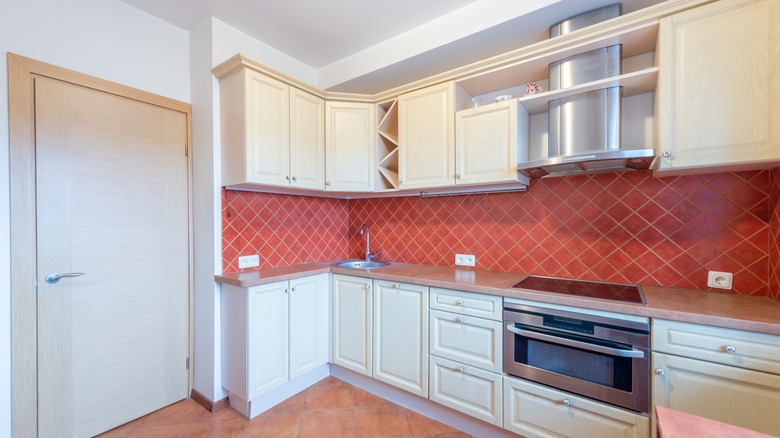 A clean kitchen with cream cabinets, red backsplash, and stainless steel appliances