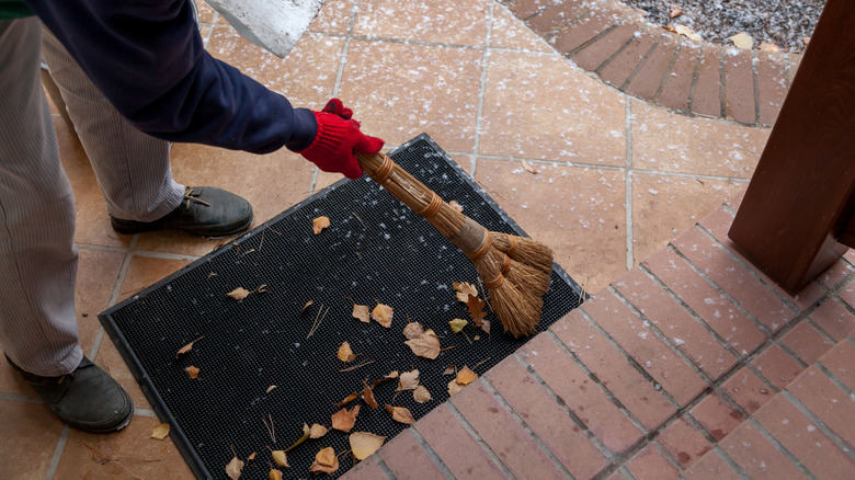 Man sweeping leaves off of doormat