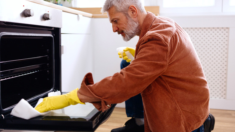 Man cleaning oven with spray and paper towel