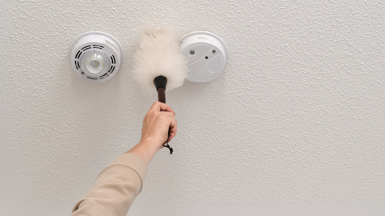 Person dusting a smoke detector on the ceiling