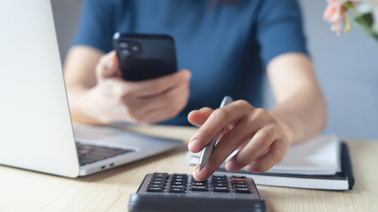 Close-up of a person using their phone and a calculator