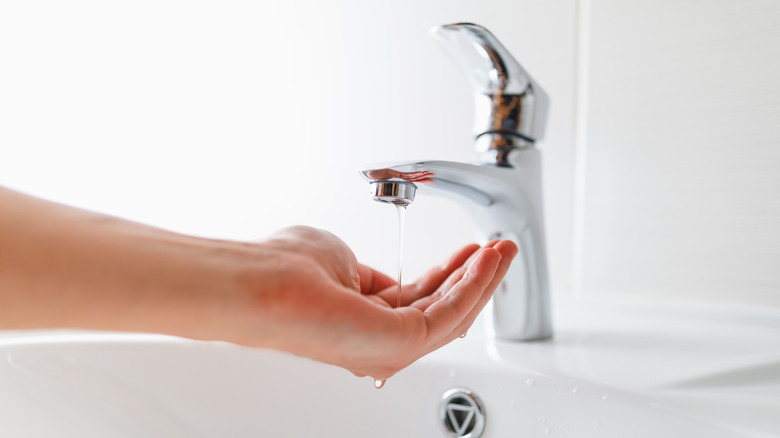 Hand under a faucet supplying a thin trickle of water