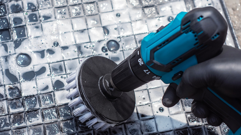 Close-up of a person using a drill and brush attachment to clean tiles and grout
