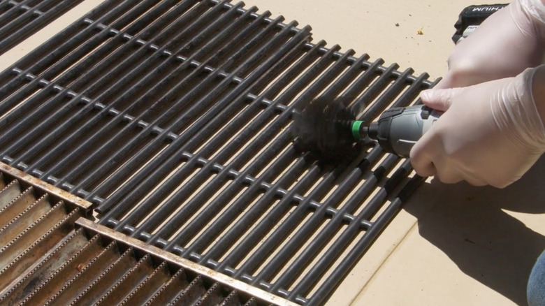 A person cleaning bbq grill grates with a drill-mounted brush