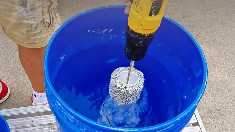 A person cleaning a paint roller with a drill attachment