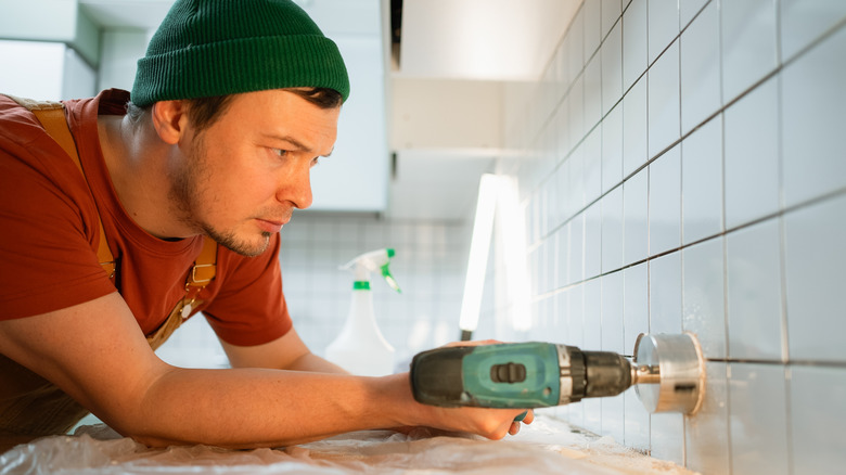 A person creating a circular hole in a tiled wall using a hole saw drill attachment