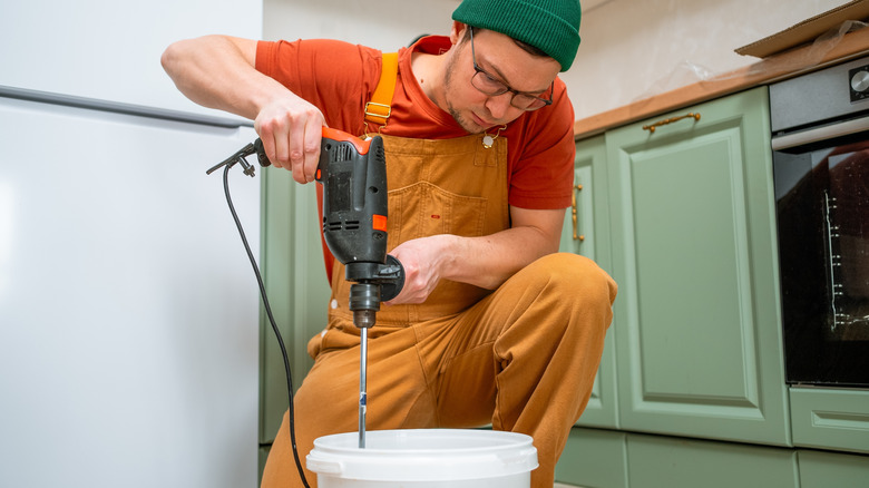 A person using a drill and mixer attachment to mix something in a bucket
