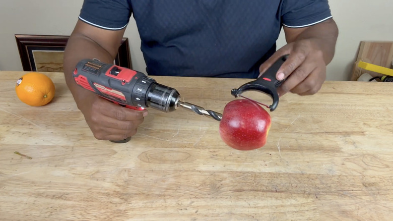 A person peeling an apple with a drill and peeler