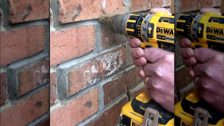 A person removing grout from between bricks with a drill attachment