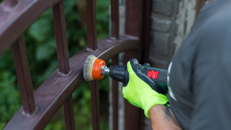A person removing rust from a metal gate with a drill and wire brush attachment