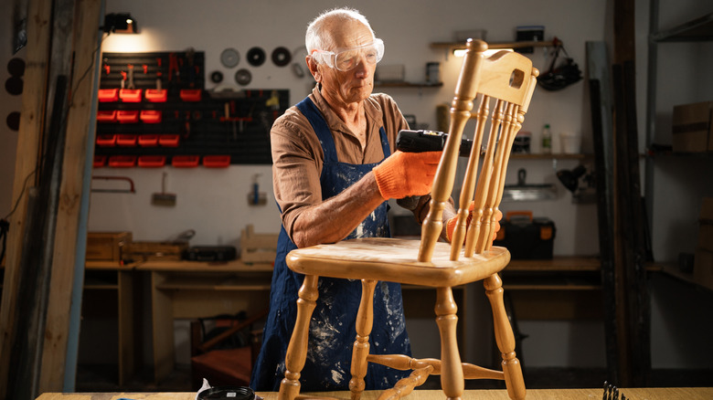 A man using a drill to sand old varnish from the spindles of a chair