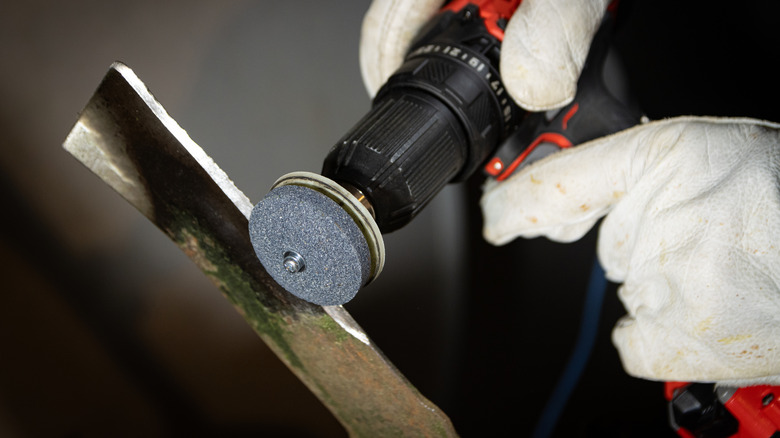 Close-up of a person sharpening a lawn mower blade with a drill and grinder attachment
