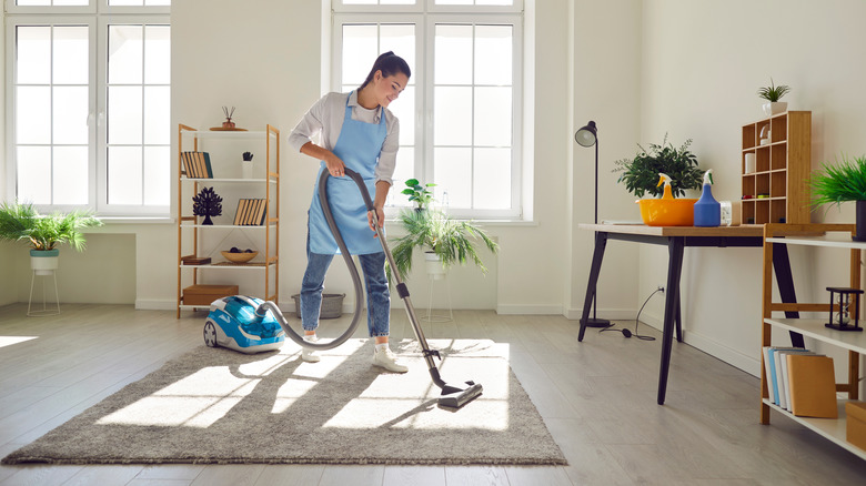 a woman wearing an apron vacuuming carpet