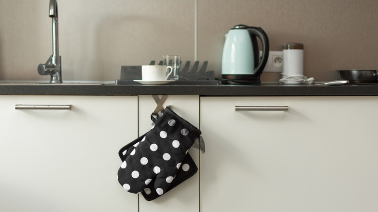 A pair of black oven mitts with white polka dots hanging on kitchen counter