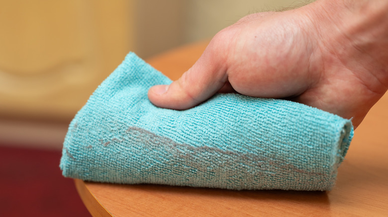 person wiping wooden surface with microfiber cloth