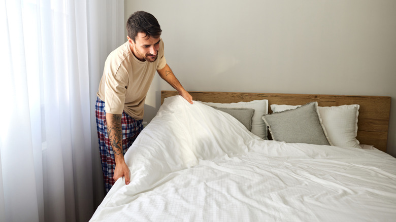 man wearing T-shirt and pajamas bottoms making bed with white sheets