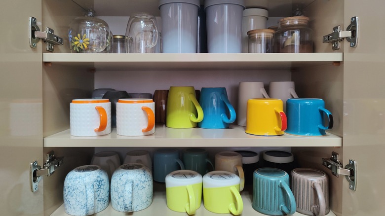 Open kitchen cabinet filled with mugs