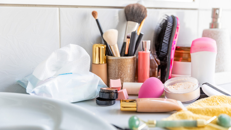 Makeup brushes, makeup, deodorant, and other personal care products by a white sink