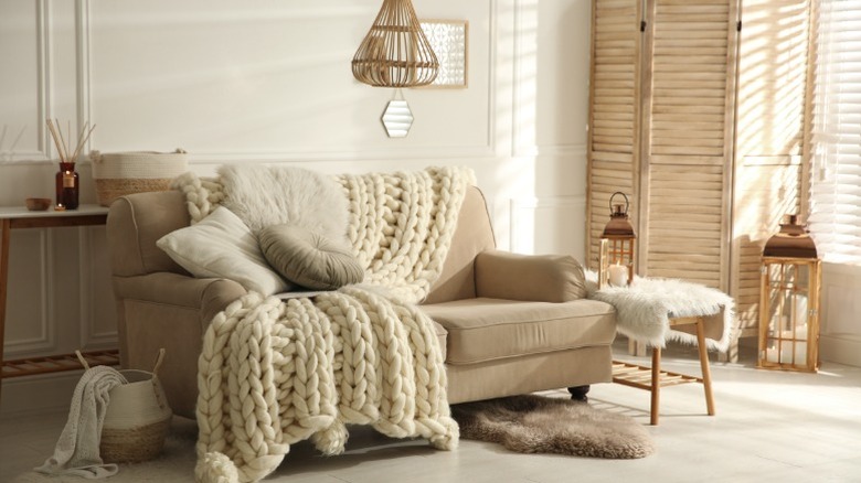 A large knit blanket draped over a couch with neutral tones