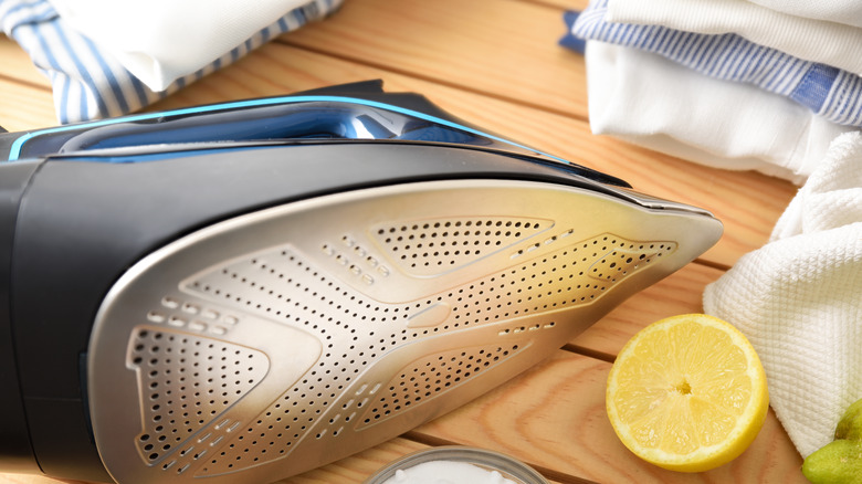 An iron lies on its side next to a halved lemon and some cloths