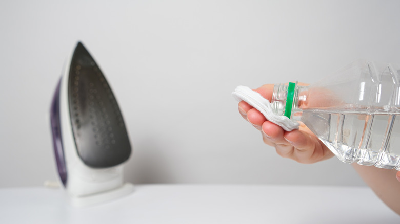 A person is pouring vinegar onto a cloth, with an iron in the background