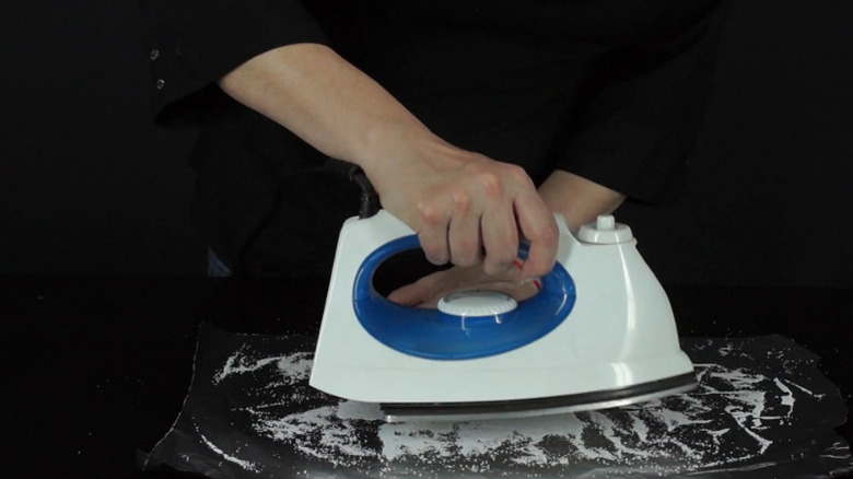 A person is running an iron over aluminum foil that's been sprinkled with salt