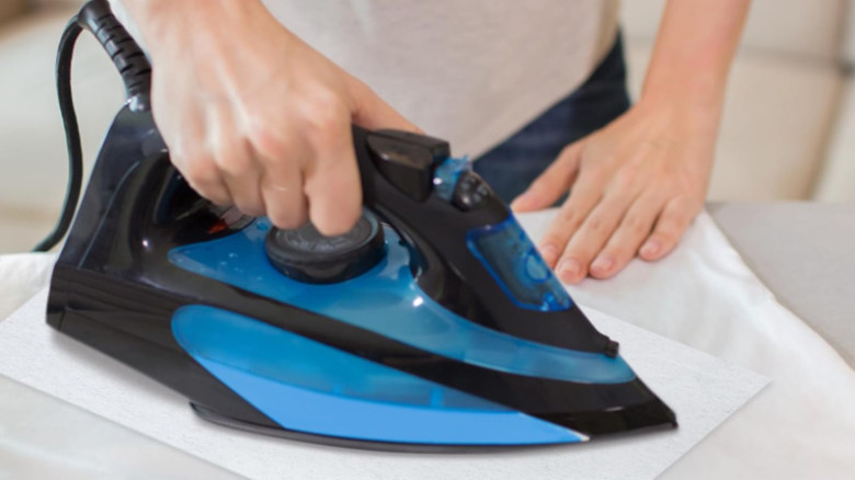 A person is seen holding an iron over a specialty cleaning cloth on the ironing board