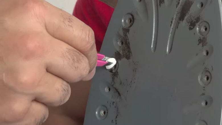 A man's hand is shown running a painkiller tablet over an iron's surface, using tweezers