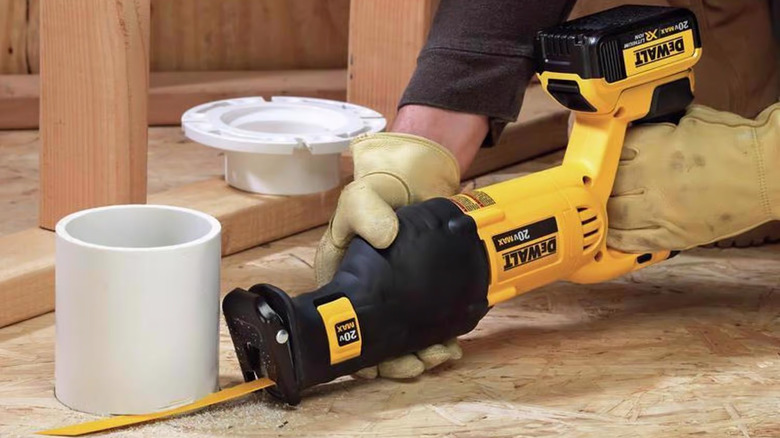 Man using DeWalt reciprocating saw to slice PVC pipe in home construction