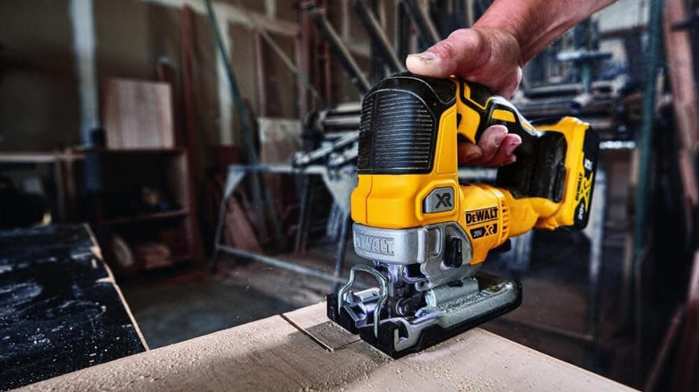 Man operating DeWalt jigsaw on wood board in wood garage workspace